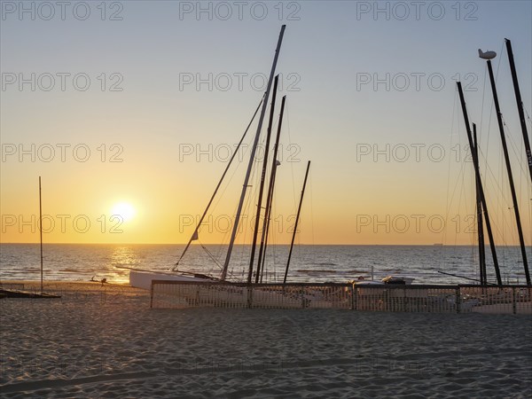 Beach with boat masts at sunset, calm and peaceful atmosphere, sand and sea, warm colours, De Haan,
