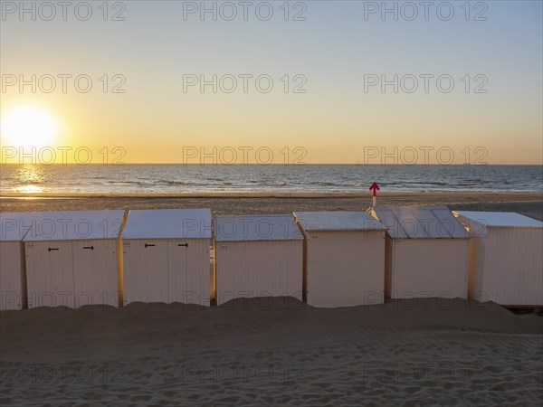 Beach with white huts, sunset over the sea, warm orange colours and calm atmosphere, De Haan,