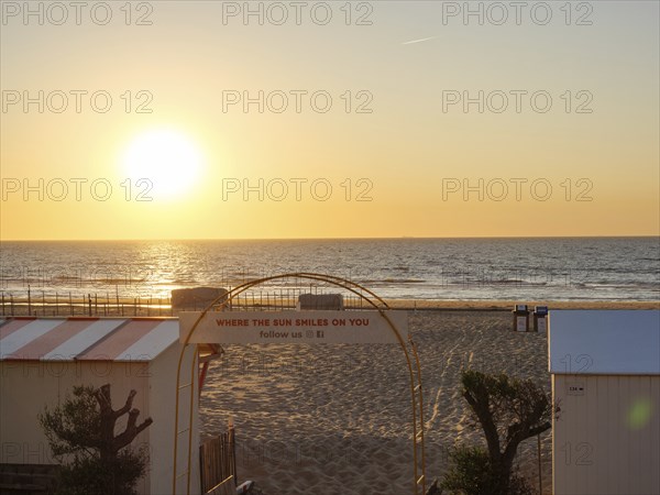 Sunset over the sea, beach with sand and an archway with lettering, quiet and peaceful atmosphere,