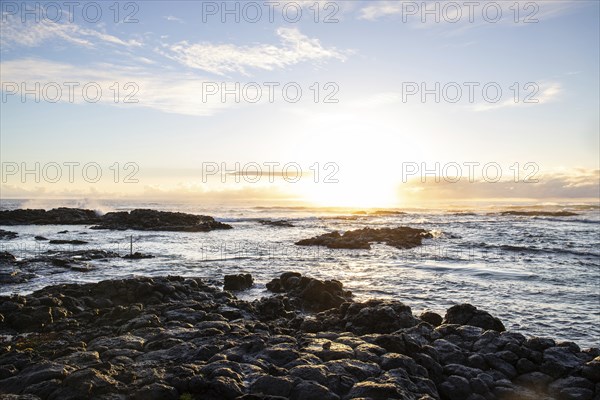 Sunrise over the sea with gentle waves. Sandy beach with lava rocks and blue water alternating with