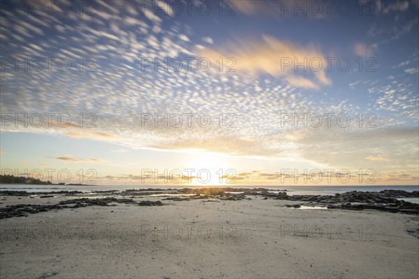 Sunrise over the sea with gentle waves. Sandy beach with lava rocks and blue water alternating with