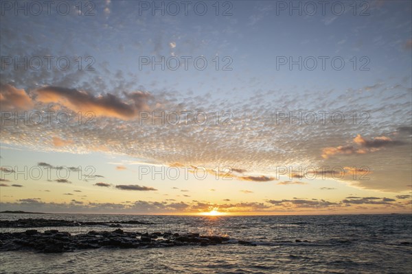 Sunrise over the sea with gentle waves. Sandy beach with lava rocks and blue water alternating with