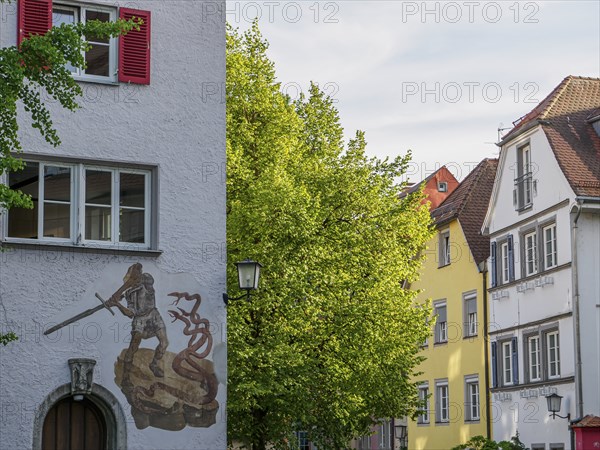 Historic building with mural of a knight and dragon surrounded by trees in an old town, lindau,