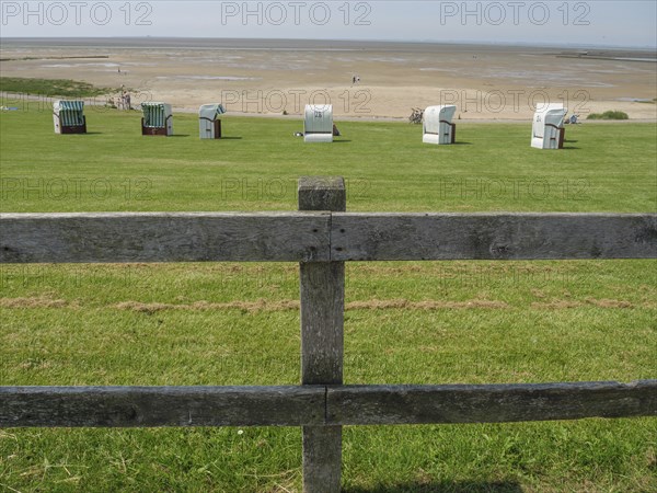 View over a green meadow with beach chairs and a wooden fence to a wide sandy beach and the sea in