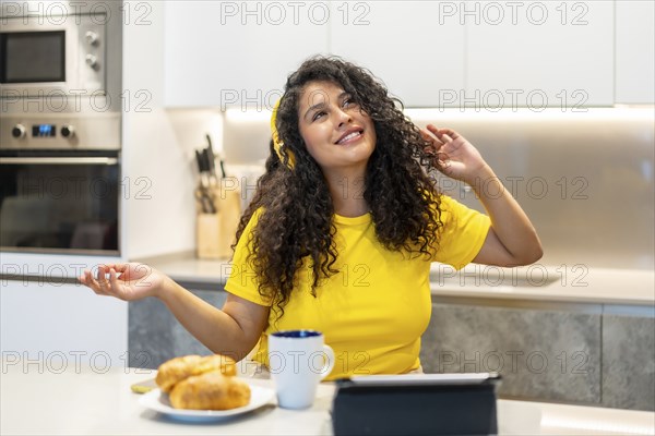 Latin happy young woman dancing while listening to music in the morning in the kitchen at home
