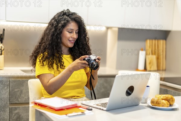 Beauty young latin female photographer checking the camera pictures working from home while eating