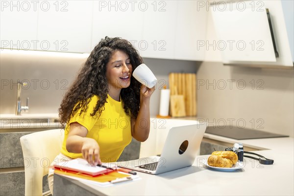 Female latin young content creator working at home while drinking coffee at morning sitting in the