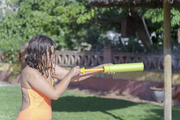 Cute girl in pink swimsuit playing in the pool with a foam gun toy