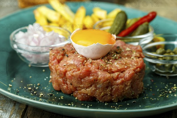 Steak tartare with open egg on wood