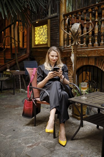 A stylish woman came to a wine bar, sat on the terrace and writes a message to her friends on her