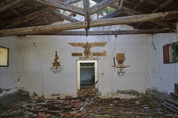 The wall of an abandoned building is covered with a peace message and several anarchy symbols,