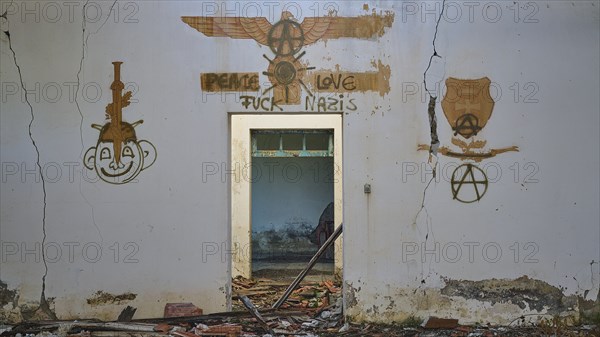 A graffiti with several artworks and a message of peace can be seen on a cracked white wall of an