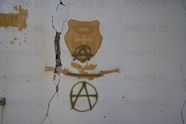 On a cracked white wall in an abandoned building, coats of arms and anarchy symbols can be seen as