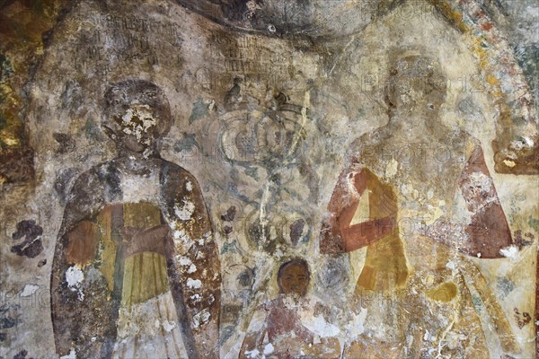 Fading frescoes on a church wall show religious figures, parents with childByzantine chapel Agios