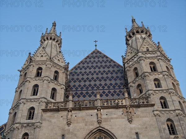 Front view of a Gothic cathedral with twin spires and a cross in the centre of the roof under a