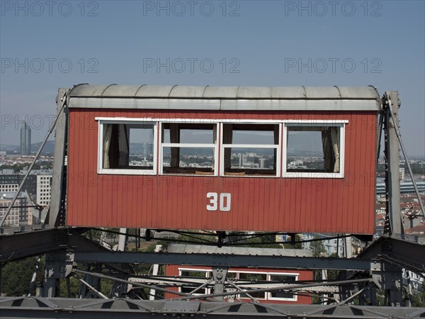 Close-up of a red cabin with the number 30 on a Ferris wheel with the city in the background,