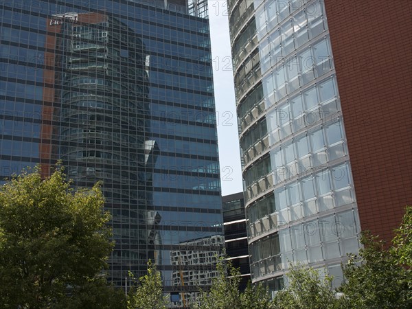 Two modern, glazed high-rise buildings with reflections and trees in the foreground, Vienna,