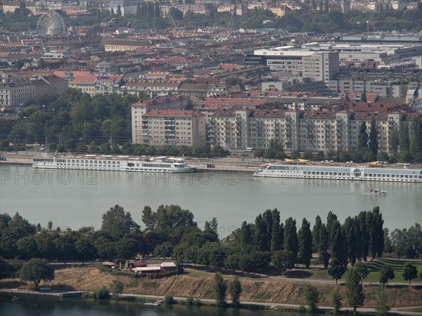 Panorama of a city by the river, lined with trees and large residential buildings in the