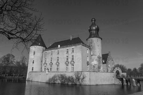 A large castle with several towers and moat reflecting in the calm water, in black and white,