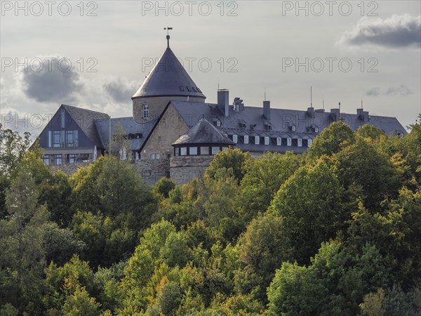 An old castle with towers surrounded by autumnal forests under a cloudy sky, Waldeck, Hesse,