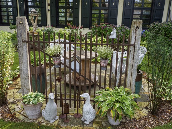 A rustic garden gate with statues and various plants surrounded by green landscape in front of a