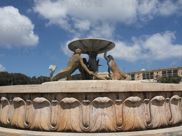 Fountain with bronze sculptures holding a bowl in front of a blue sky, valetta, mediterranean sea,
