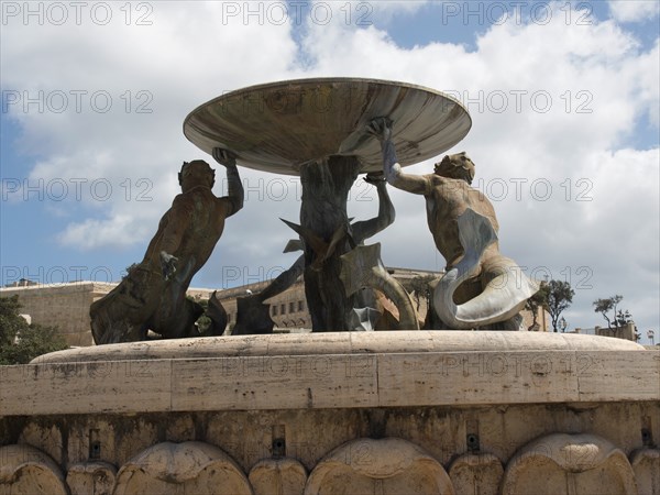 Bronze sculptures holding a large bowl of a fountain in a public square, valetta, mediterranean
