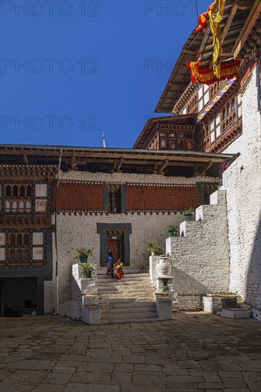 Two happy Bhutanese kids in colorful clothes walking up the stairs in the backyard of Trongsa