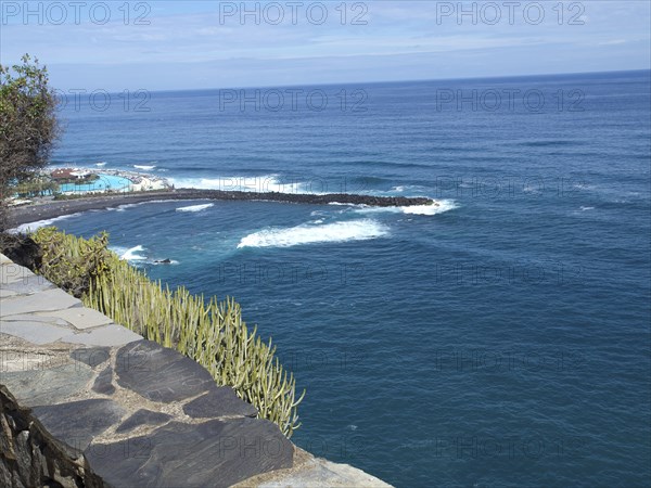 View of the vast sea and the waves lapping against the shore under a blue sky, Puerto de la cruz,