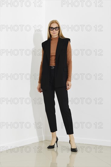 Stylish professional woman in chic black vest, terracotta sweater and tailored trousers, standing