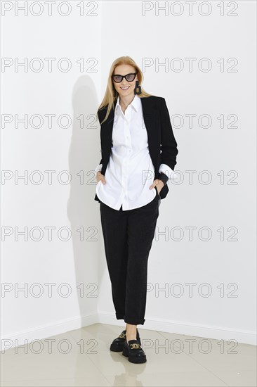 Slim beautiful blonde business woman standing near white office wall in casual black suit. Concept