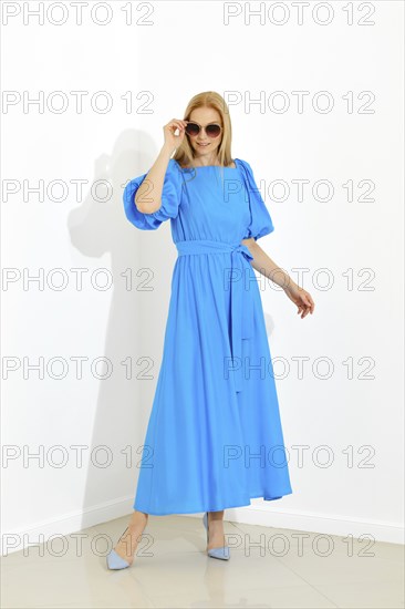 Dynamic full-length portrait of a woman in a bright blue dress and matching shoes against a white