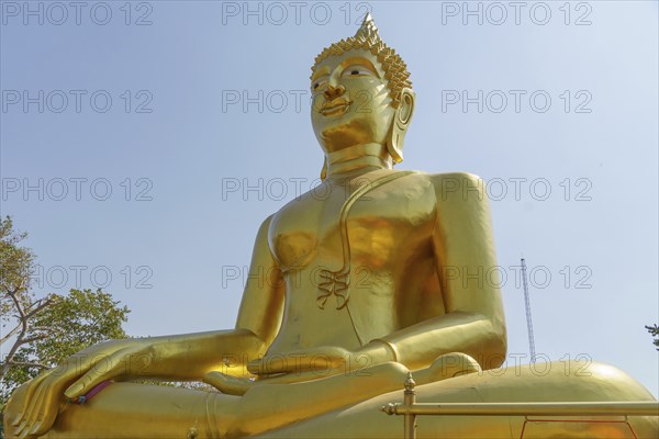 Large golden Buddha statue in lotus position in front of clear sky and trees, Pattaya, Thailand,