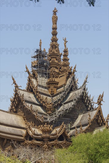Detailed wooden temple with numerous sculptures and artistic elements against a blue sky, Pattaya,