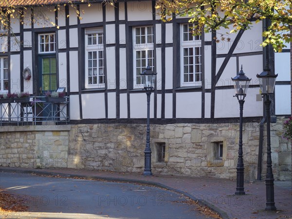 A historic half-timbered house with lanterns on a quiet street, surrounded by autumn trees and
