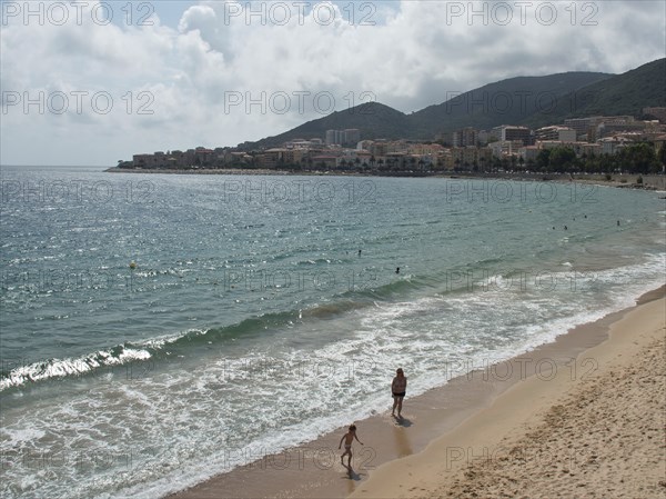 People walking along a sandy beach with a coastal town in the background, ajaccio, corsica, france