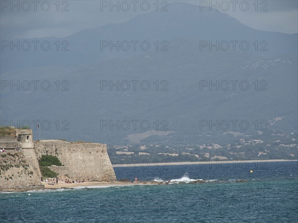 Ancient fortress wall on the coast with a view of the sea and cloudy mountains in the background,