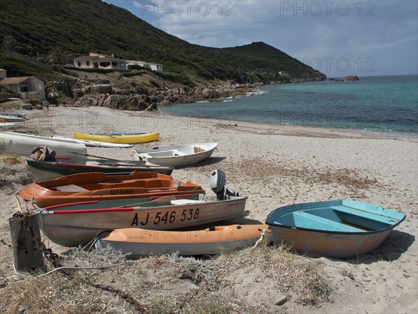Several boats moored on the sandy beach in front of emerald green sea and green coastal hills,