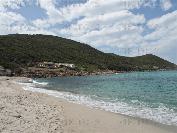 A wide sandy beach meets the clear blue sea with green hills and houses in the background, ajaccio,
