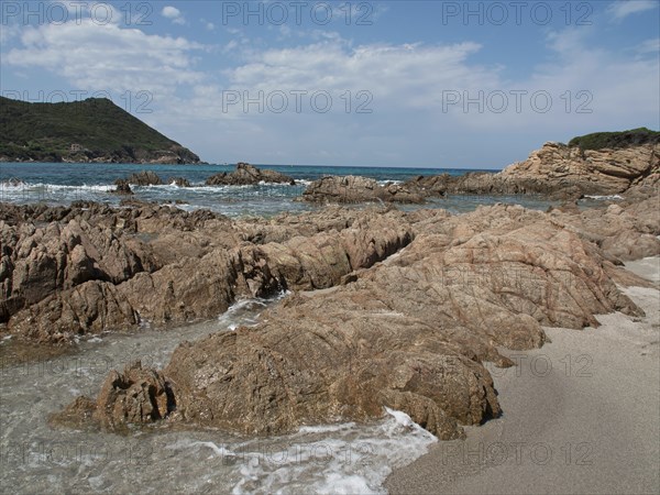 Rocky shoreline with smaller waves reaching the shore under a blue sky, ajaccio, corsica, france