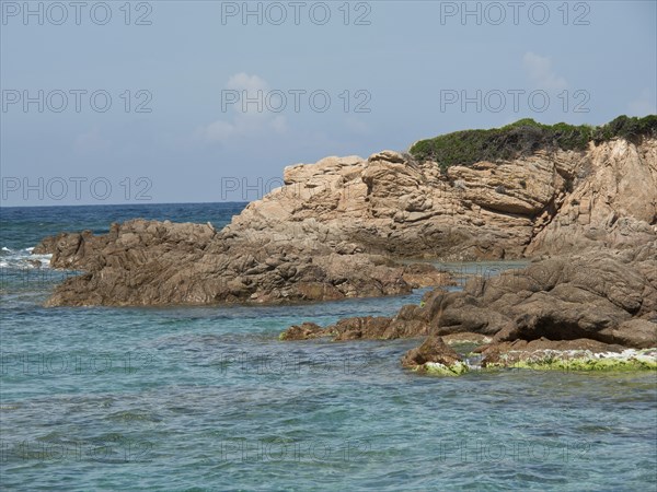Rough rocky coast lapped by turquoise sea under a slightly cloudy sky, ajaccio, corsica, france
