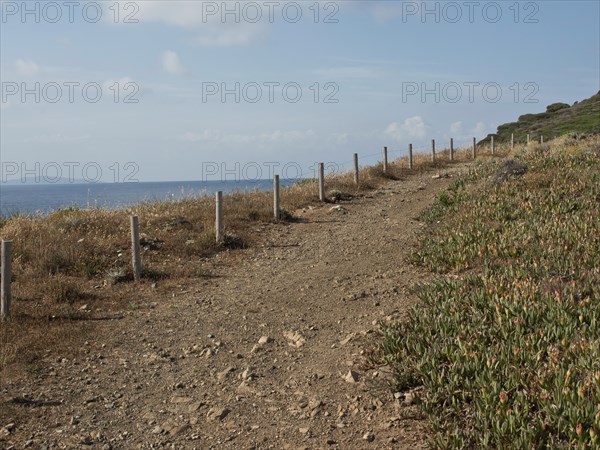Path along a coastline with railings, plants and a view of the sea under a blue sky, ajaccio,