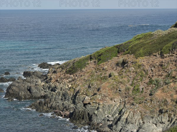 Coastal landscape with rocky shore and green vegetation, the sea is calm and the sky is blue,