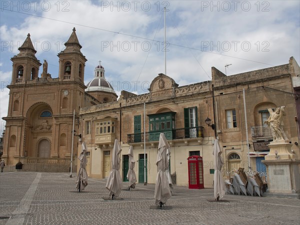 A historic square with a large church and surrounding buildings under a cloudy sky, marsaxlokk,