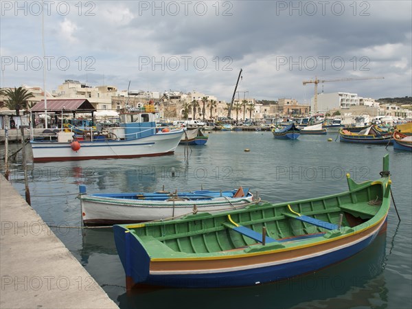 Colourful boats in the harbour overlooking a small town, under a cloudy sky, marsaxlokk,