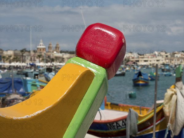 A colourful detail of a boat with a busy harbour and town in the background, marsaxlokk,