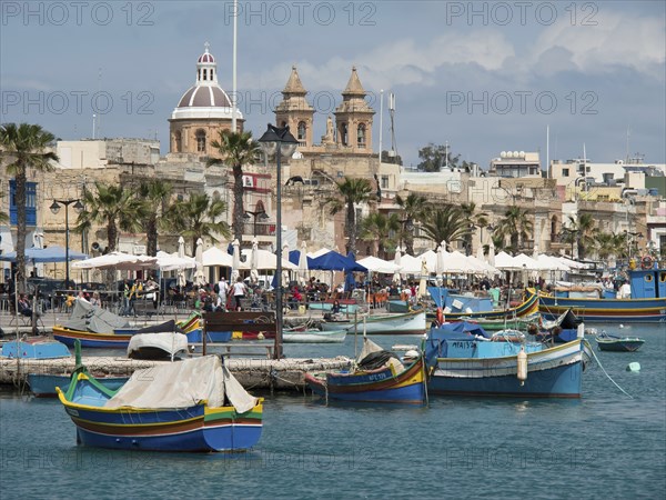 Lively harbour with colourful boats, palm trees and historic churches in the background,