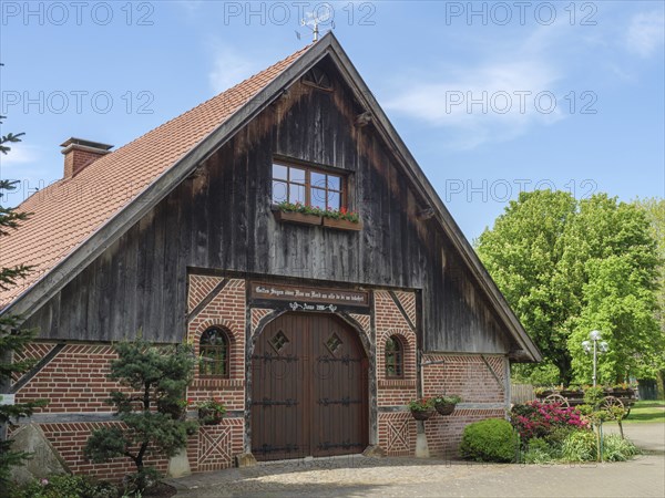 Rustic barn made of wood and brick with flowers and plants in the foreground under a blue sky,