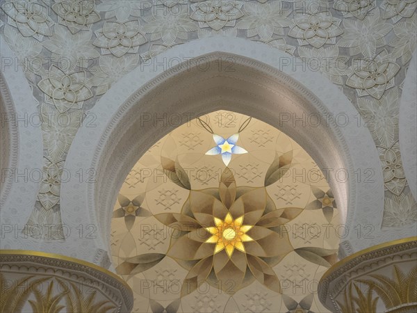 Ornate ceiling with intricate patterns and symmetrical design illuminated by beams of light, abu