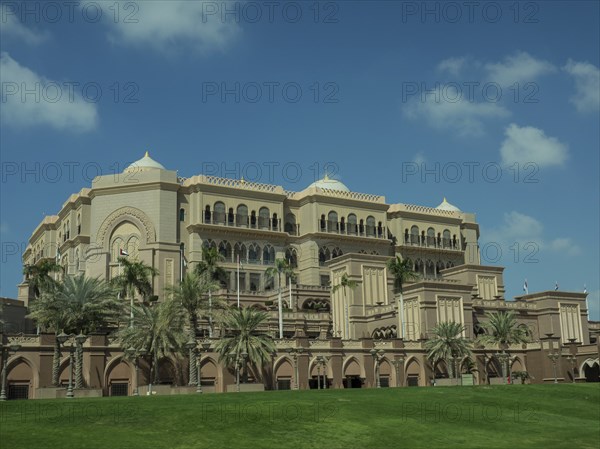 Magnificent palace with palm trees and green lawn under a clear sky, abu dhabi, united arab